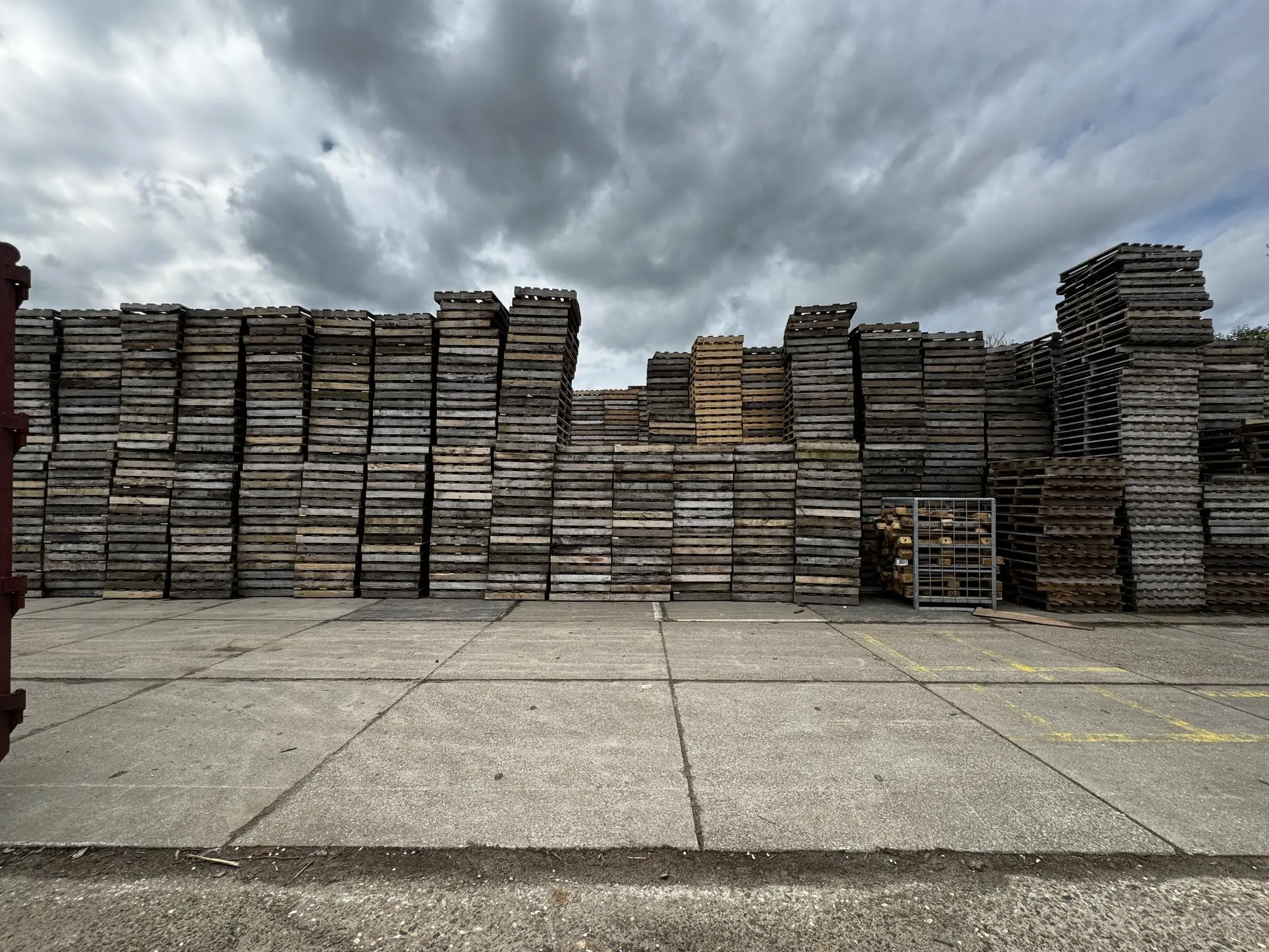 Hoge stapels houten pallets en kratten op een industrieterrein aan de Graaf van Lynden van Sandenburgweg onder een bewolkte lucht.